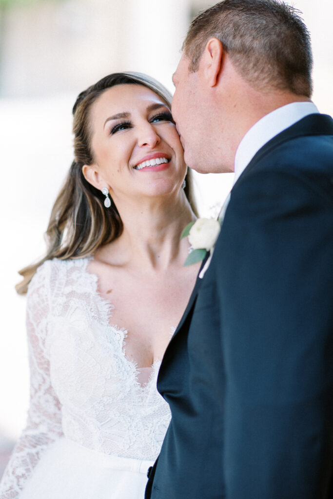 Groom gently kisses his bride on the cheek during their romantic wedding at Aster Café in Minneapolis, capturing a timeless and intimate moment.