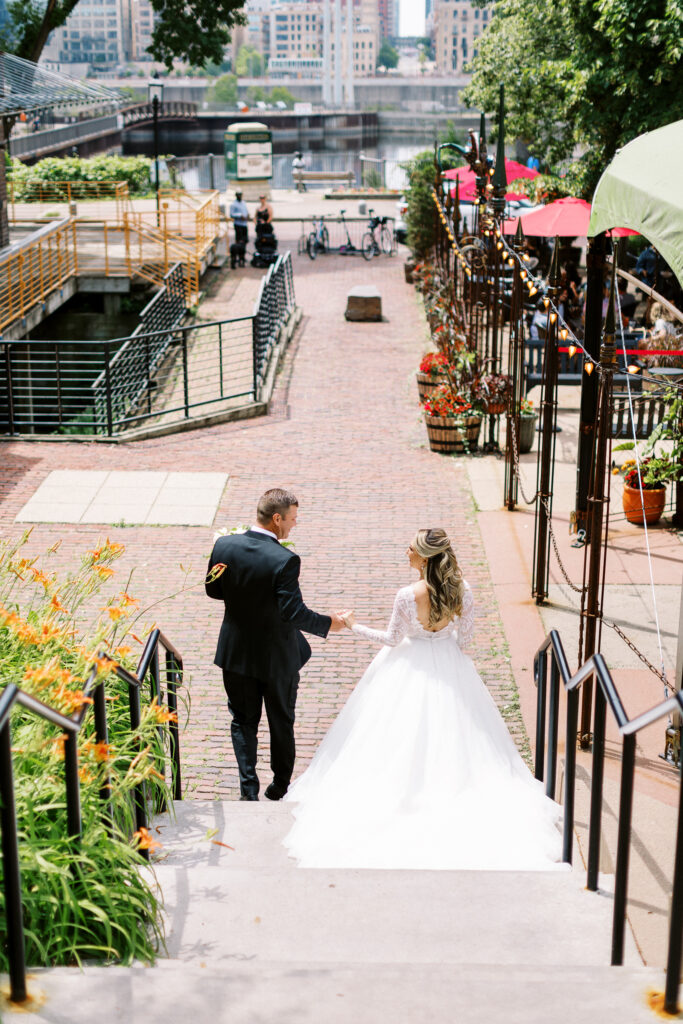 Bride and groom are walking down the steps of the Aster Cafe with the bride in her beautiful wedding gown and groom in his tuxedo. They're holding hands together as they walk.