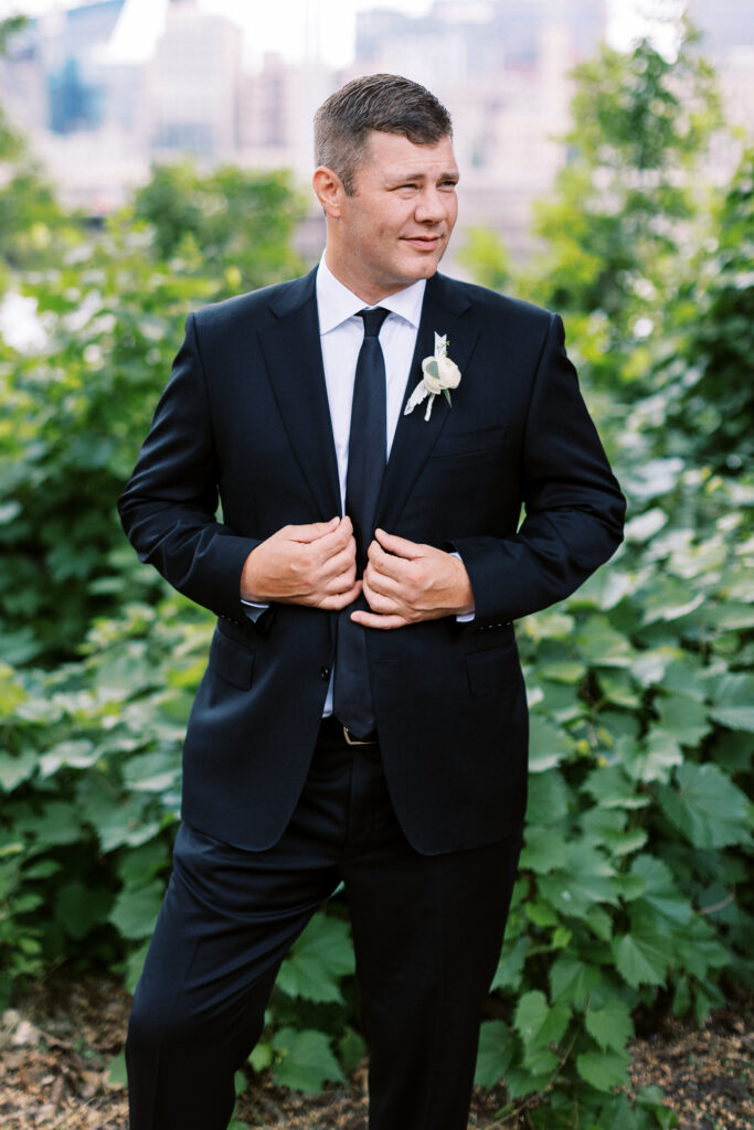 Groom wearing a black Prada suit in front of the Minneapolis skyline. 