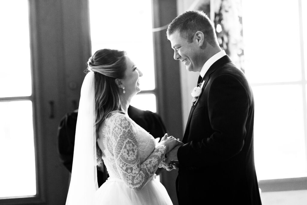 Groom and bride at their ceremony holding hands and looking at each other with joy.