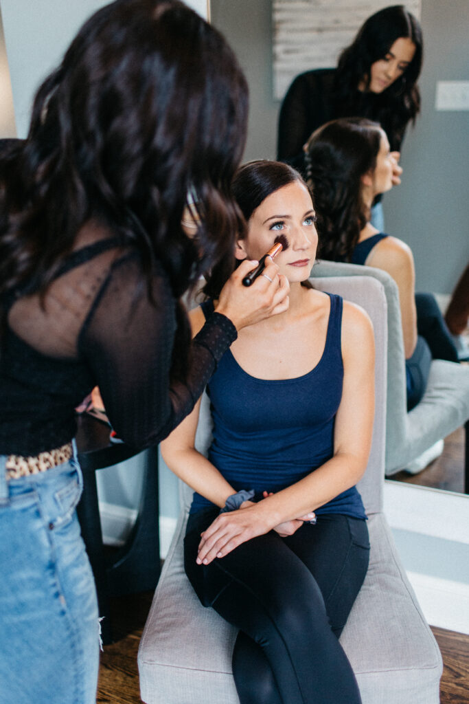 The bride is in front of a mirror while her makeup is being done.