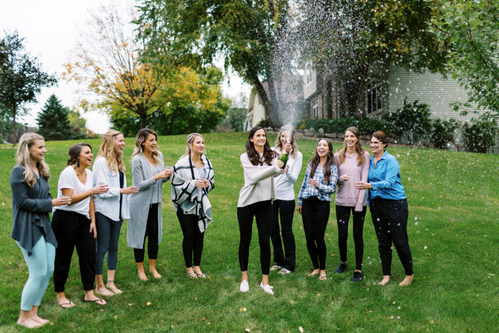 The bride and her bridesmaids popping a bottle of champagne.