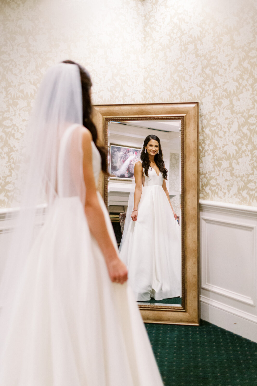 A bride with happy tears in her eyes looks at herself in a mirror at Bearpath Golf and Country Club in her stunning white wedding dress.