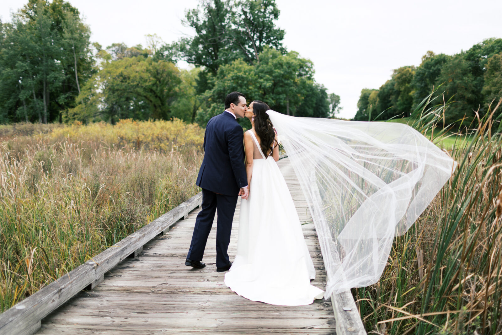 Bride and groom kissing on the boardwalk with her long vail flowing. 