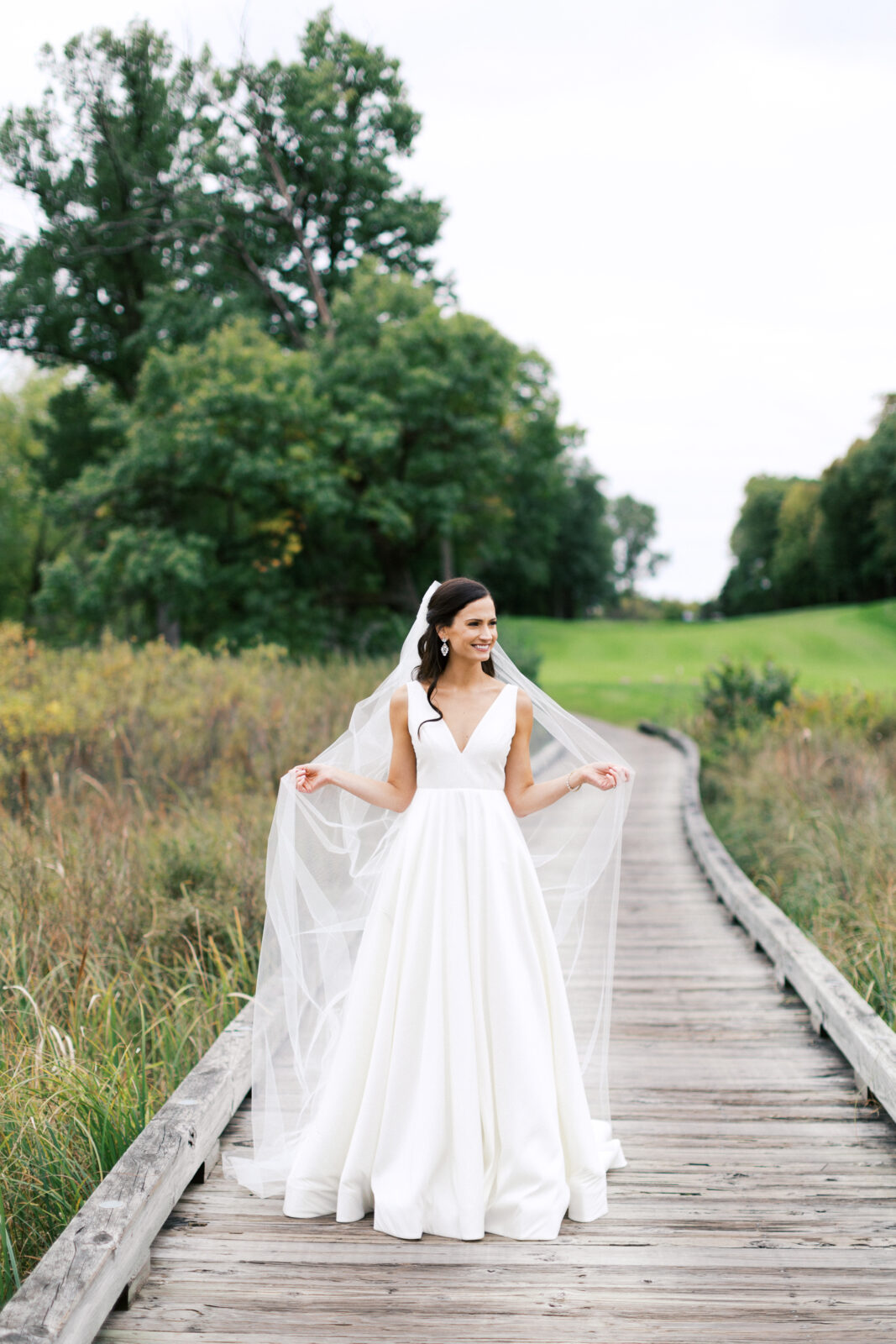 Bride is posing for a photo looking away with a long vail in her hands.
