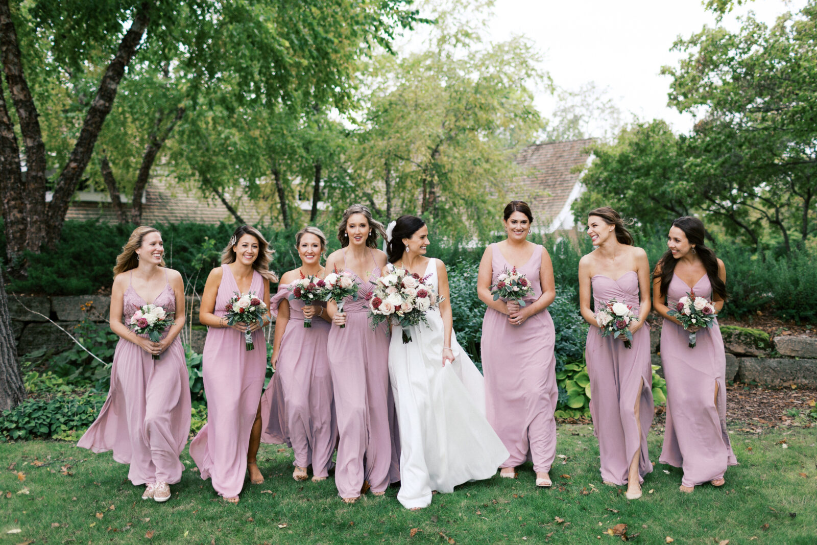 Bridesmaids walking through the grass looking at eachother and laughing. Bearpath Golf and Country Club.