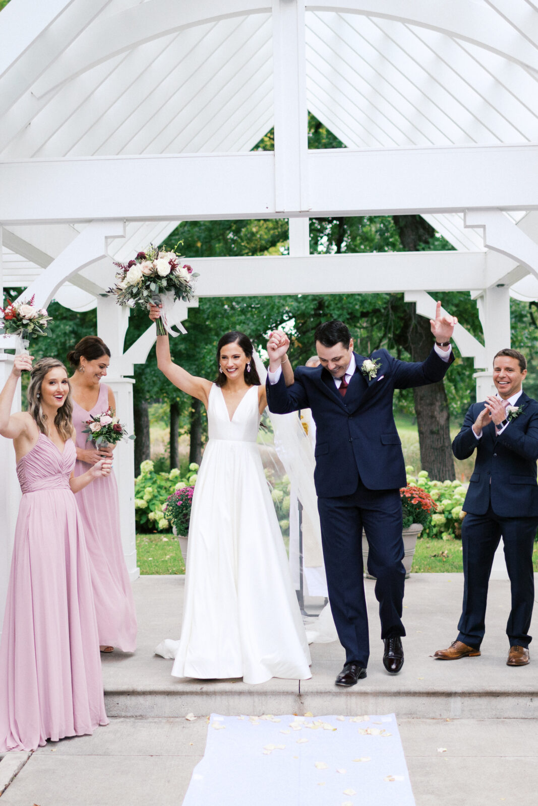 Husband and wife celebrate their wedding. The photo shows the newly married couple standing on stage together as they throw their hands up in the air. The couple is happy and in love.