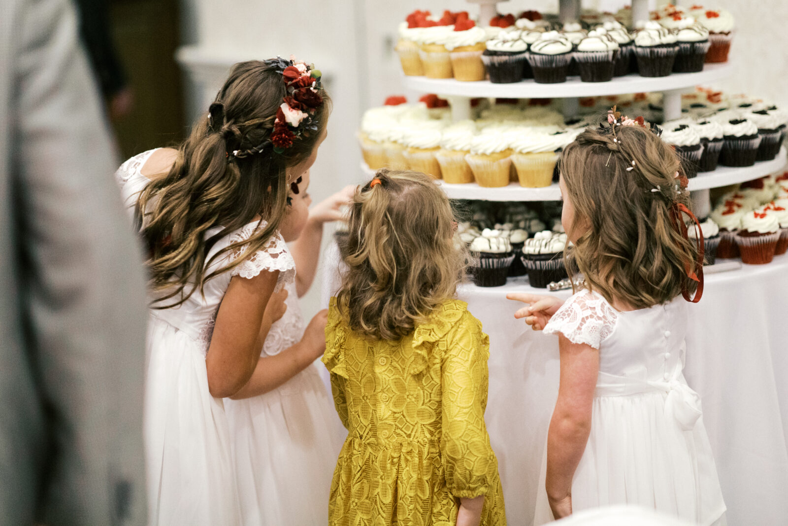 Girls gently touch one of the cupcakes at a stand filled with cupcakes.