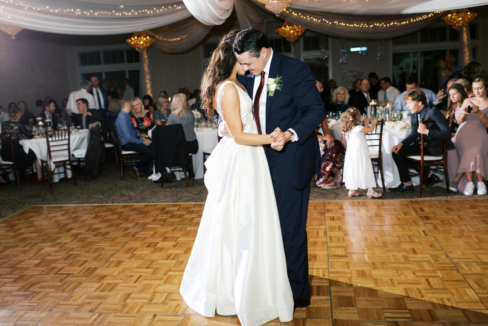 The bride and groom are dancing at their wedding reception. They are hugging each other and smiling.