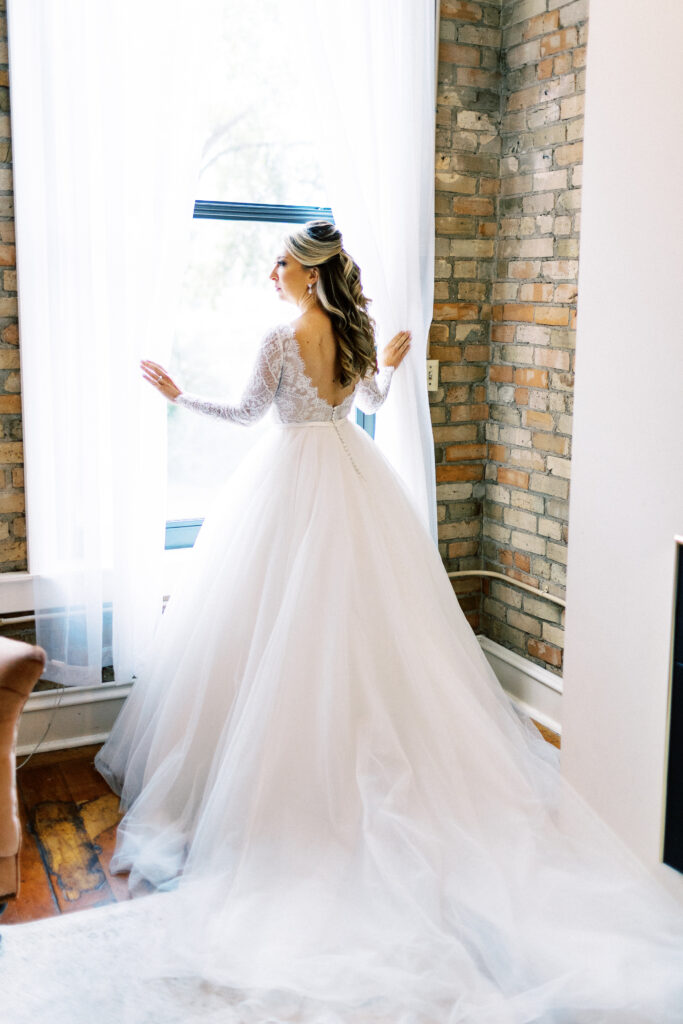 The bride is looking in the window in her wedding dress at Aster Weddings & Events wedding