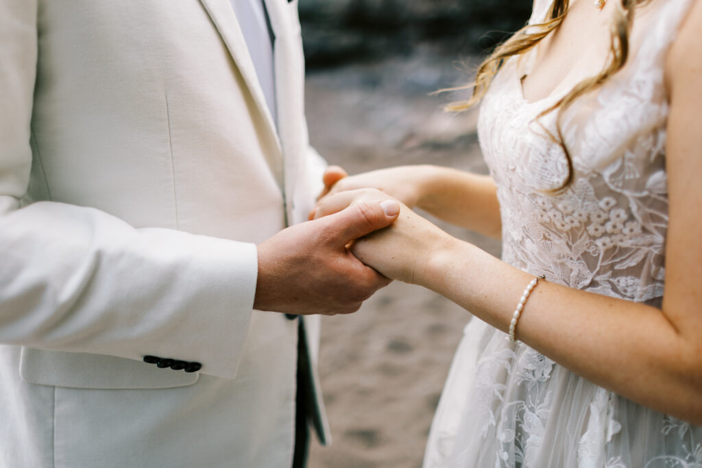 A groom holding his bride's hands at a wedding on the shores of Lake Superior, a part of Minnesota's North Shore.