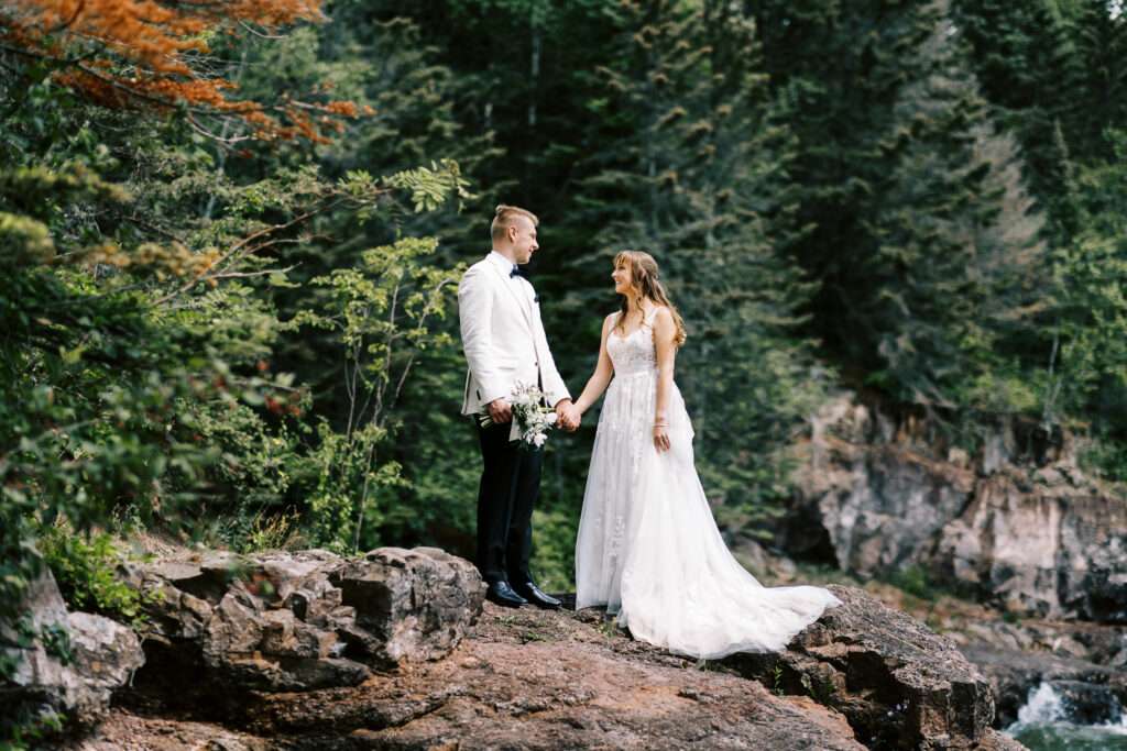 Bride and groom standing and holding hands on the cliff of North shore on the lake Superior. Captured by the top wedding photographer Toly Dzyuba Photography. 