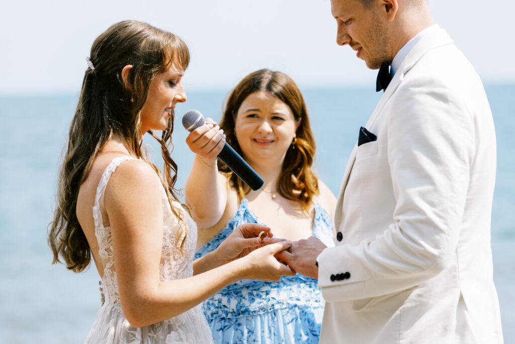 Toly Dzyuba Photography captures a North Shore wedding in Minnesota where the bride and groom are exchanging their rings on the shore by the lake. The bride has a big smile on her face. Photographed by Toly Dzyuba Photography.