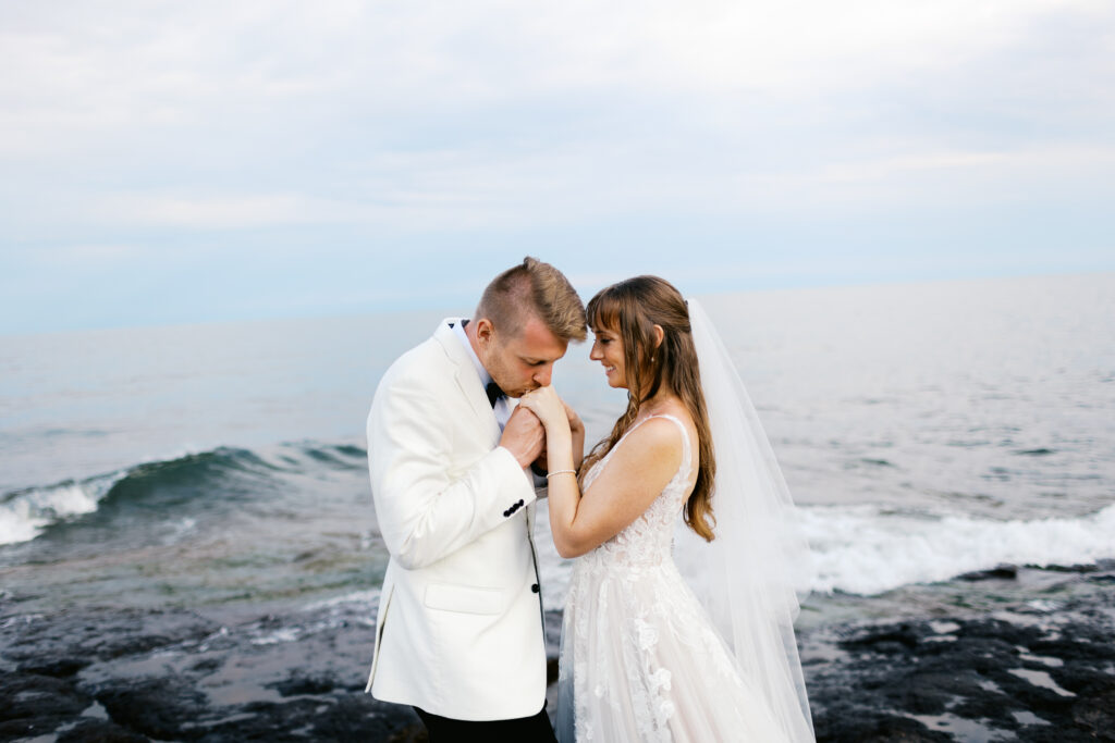 Groom kissing her hands and standing on the rocks of North Shore.