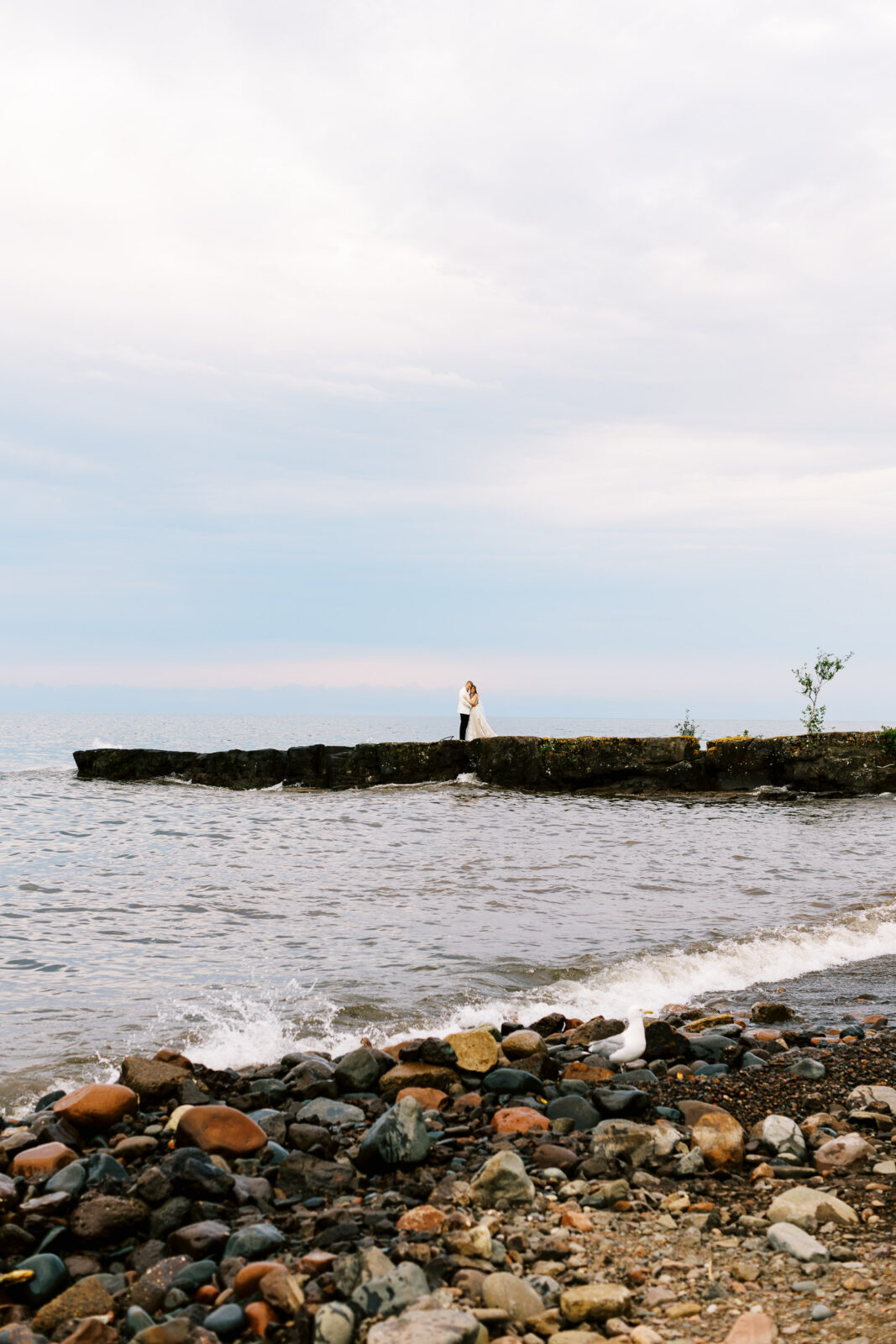 Groom and bride embracing while standing on a rock along the North Shore of Lake Superior.