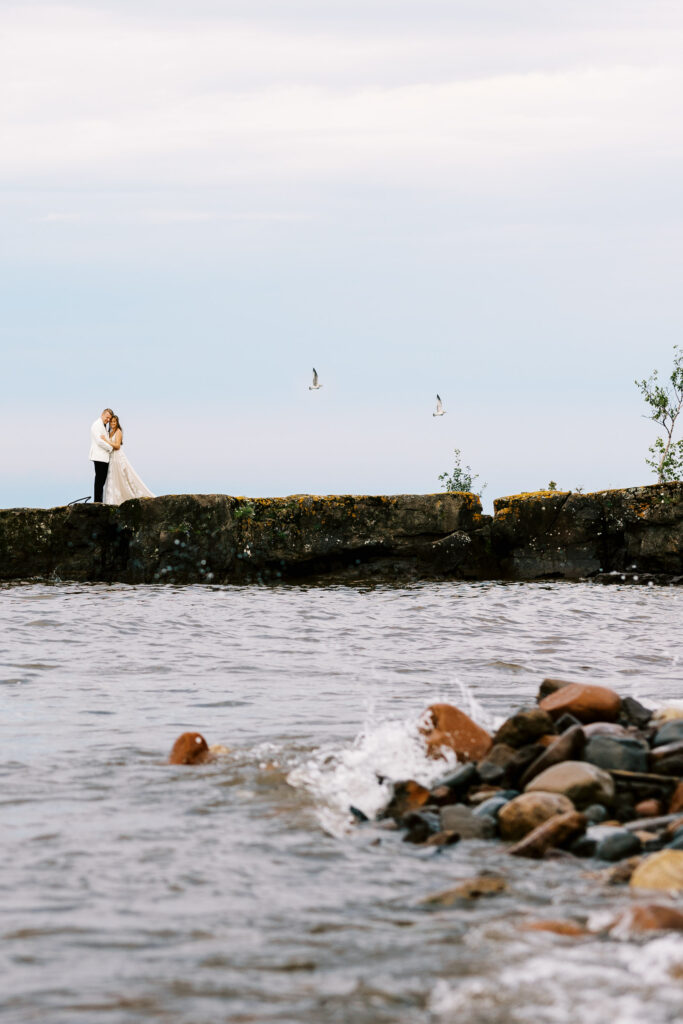 Groom and bride embracing while standing on a rock along the North Shore of Lake Superior.