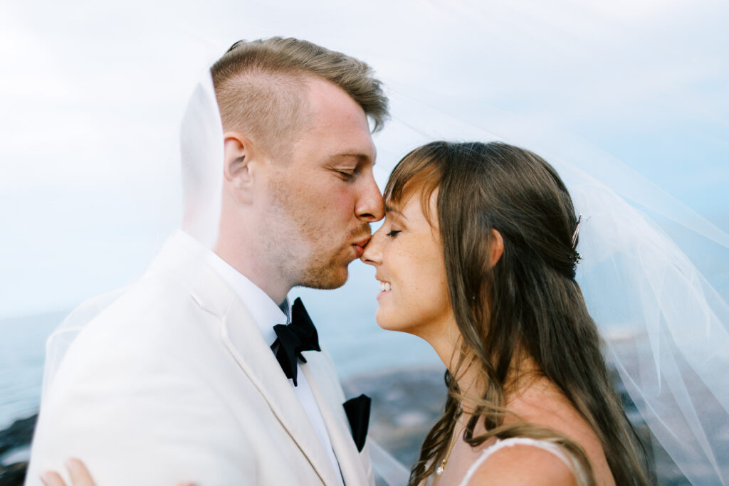 Groom gently kissing the bride's nose while standing on a rock along the North Shore of Lake Superior.