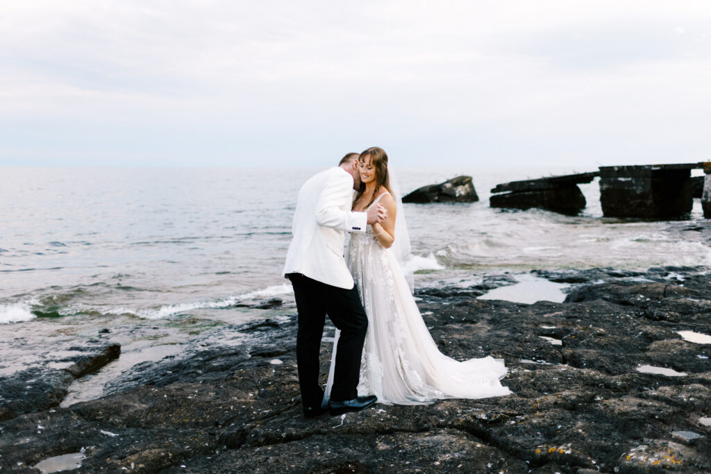 Groom kissing his bride's shoulder on the beach of North Shore