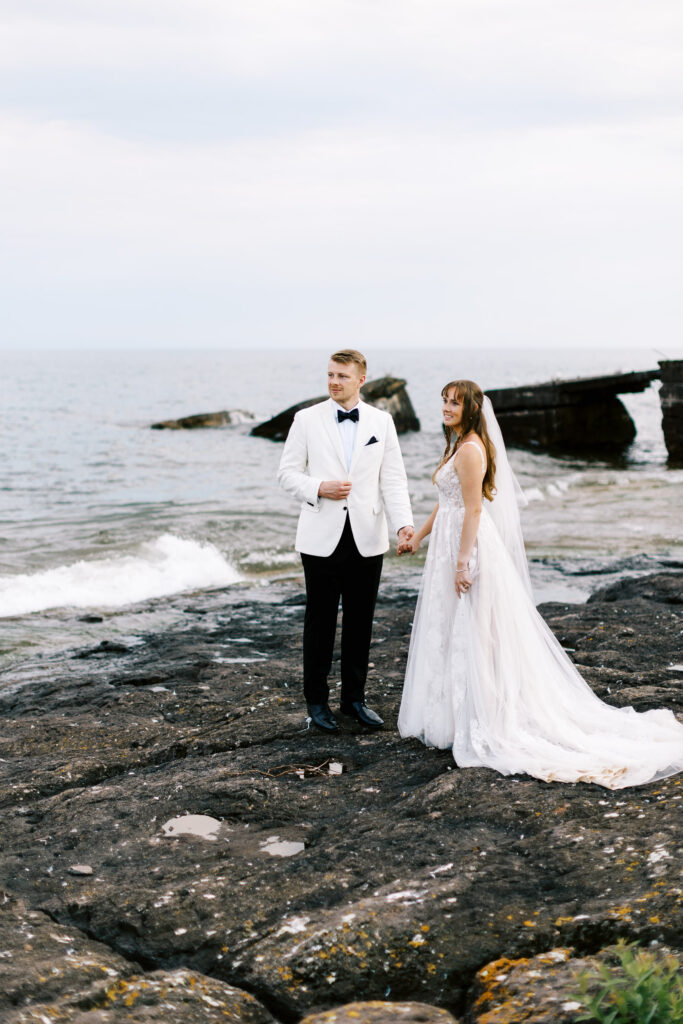 Toly Dzyuba Photography capturing bride and groom on the rocks of Lake Superior looking away.