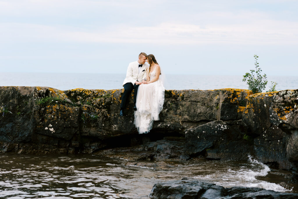 Bride and groom sitting on the rock of North Shore with their foreheads touching.