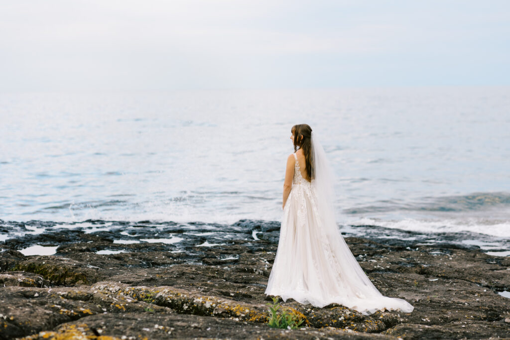 North Shore wedding at Bluefin Bay Resort. The bride is posing for a photo on the rocks while waves crash in around her.