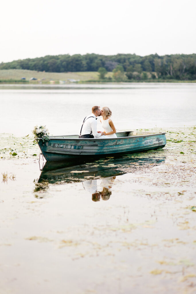 Groom on the lake is kissing his bride while in the boat.