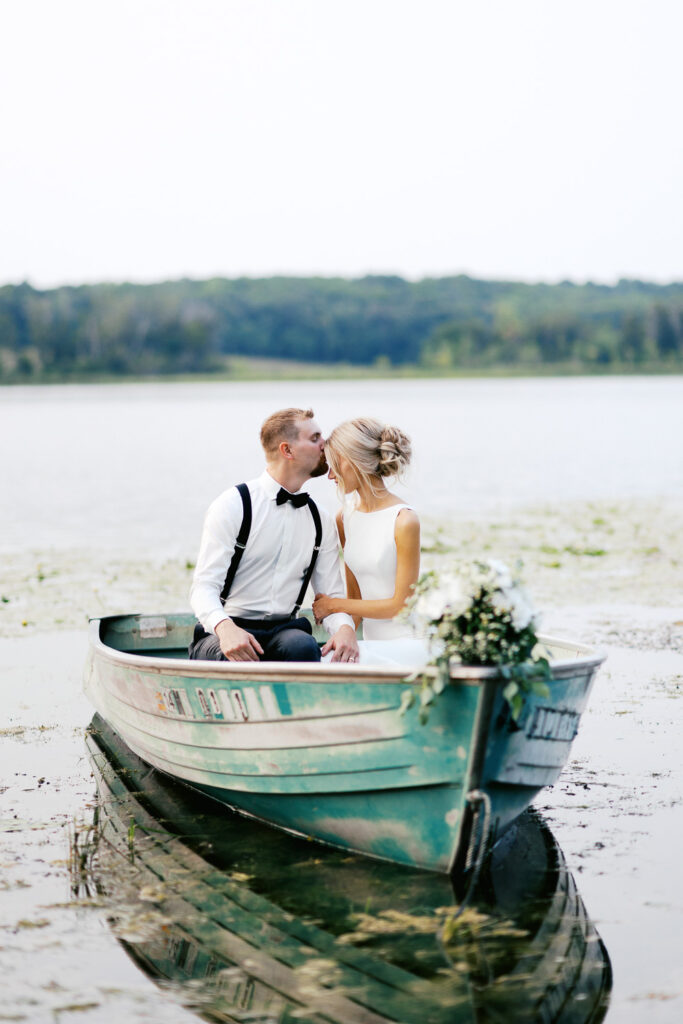 Groom in the boat kissing her forehead on Detroit Lakes in a boat, surrounded by the serene beauty of nature.