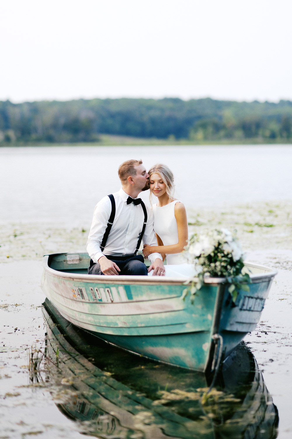 Intimate moment of Groom kissing the bride's head in the boat on a lake at sunset.