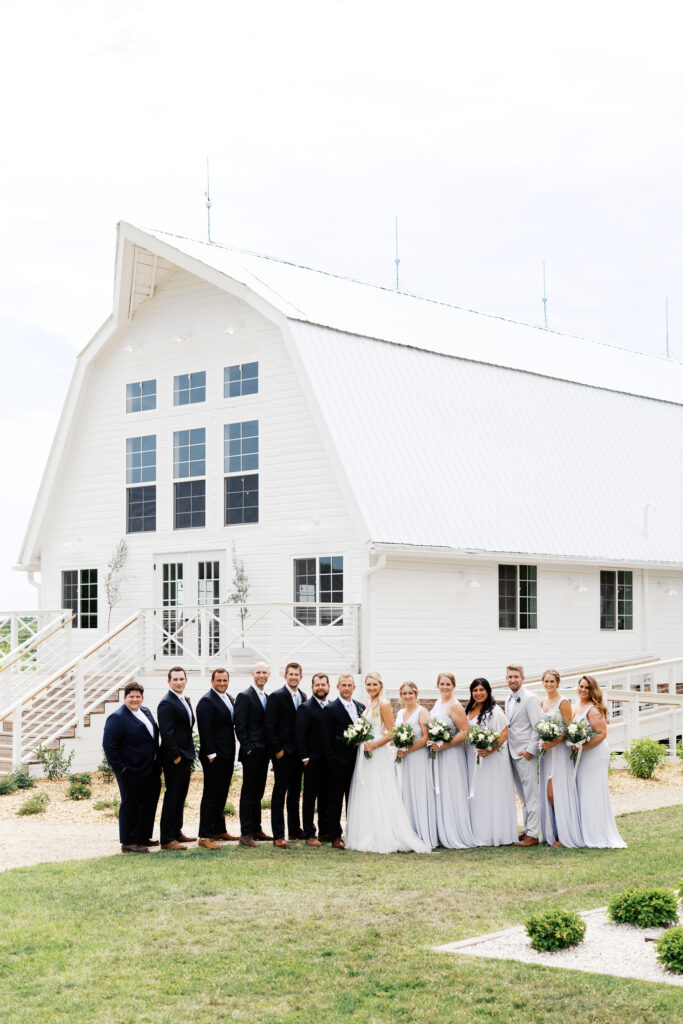 This is a portrait of the wedding party at Ivory North Co. The rustic white barn is in the background.