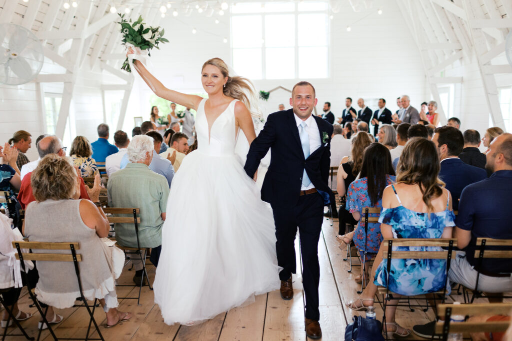 The bride and groom are celebrating their just-completed wedding ceremony as they exit Ivory North Co. The bride is wearing a white dress and veil, and the groom is wearing a dark suit.