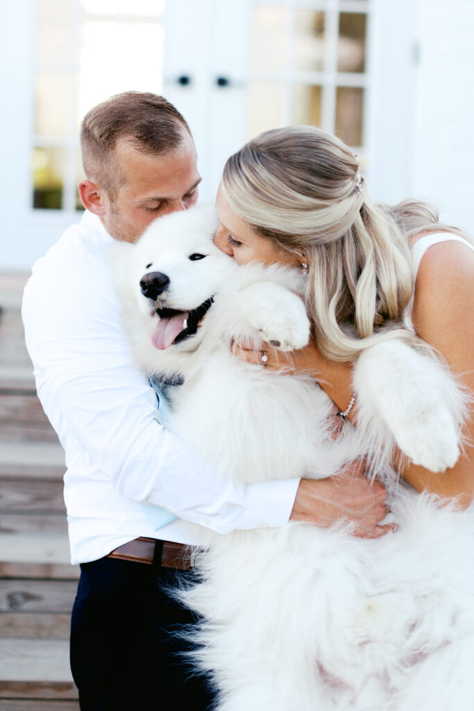 Newlyweds kissing their Samoyed dog on their wedding.  By Toly Dzyuba Photography.