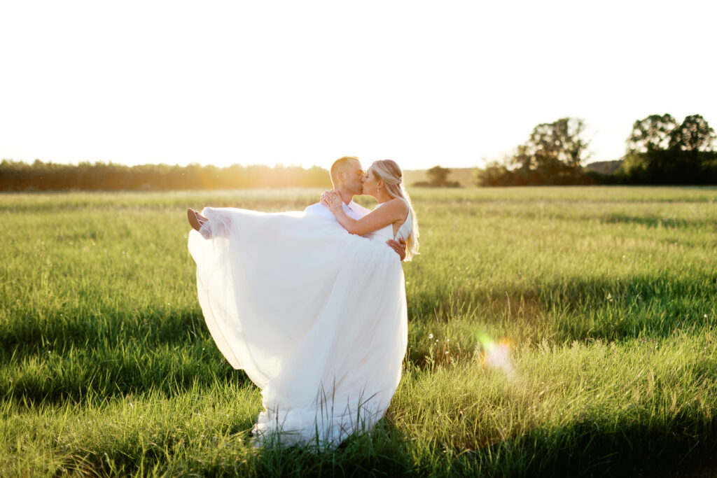 Newlyweds kissing with sunset glowing on the back. By Toly Dzyuba Photography.