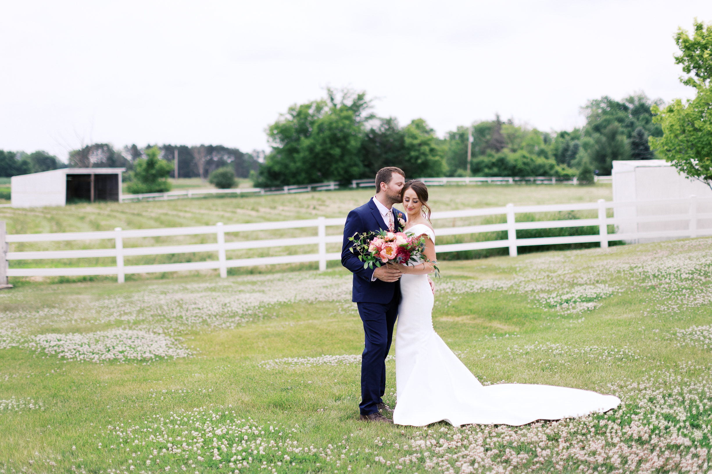 Bride and groom standing on the green field kissing his bride at Abella weddings and events