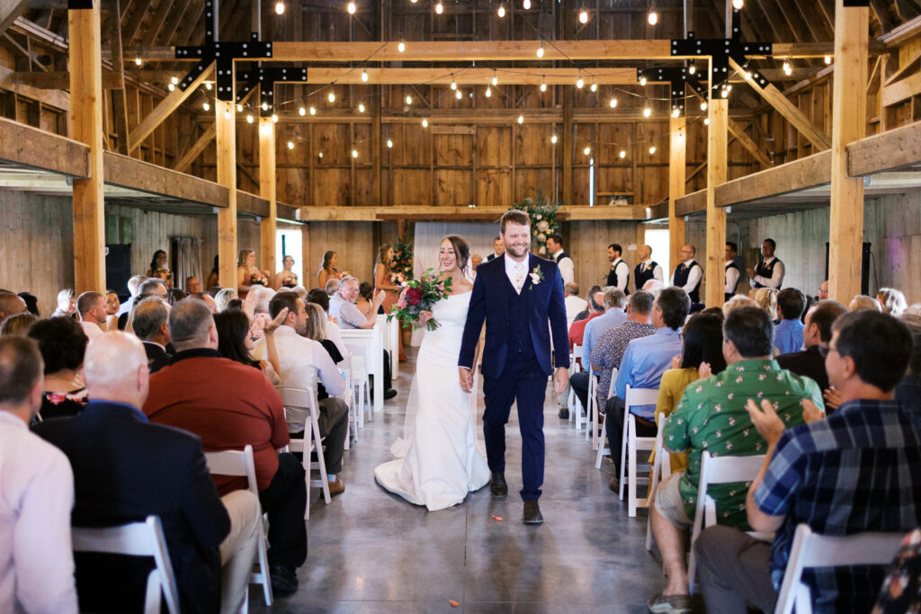 Newlyweds joyfully exiting their ceremony inside the barn at Abella Weddings and Events in Minnesota, photographed by a Minnesota wedding photographer
