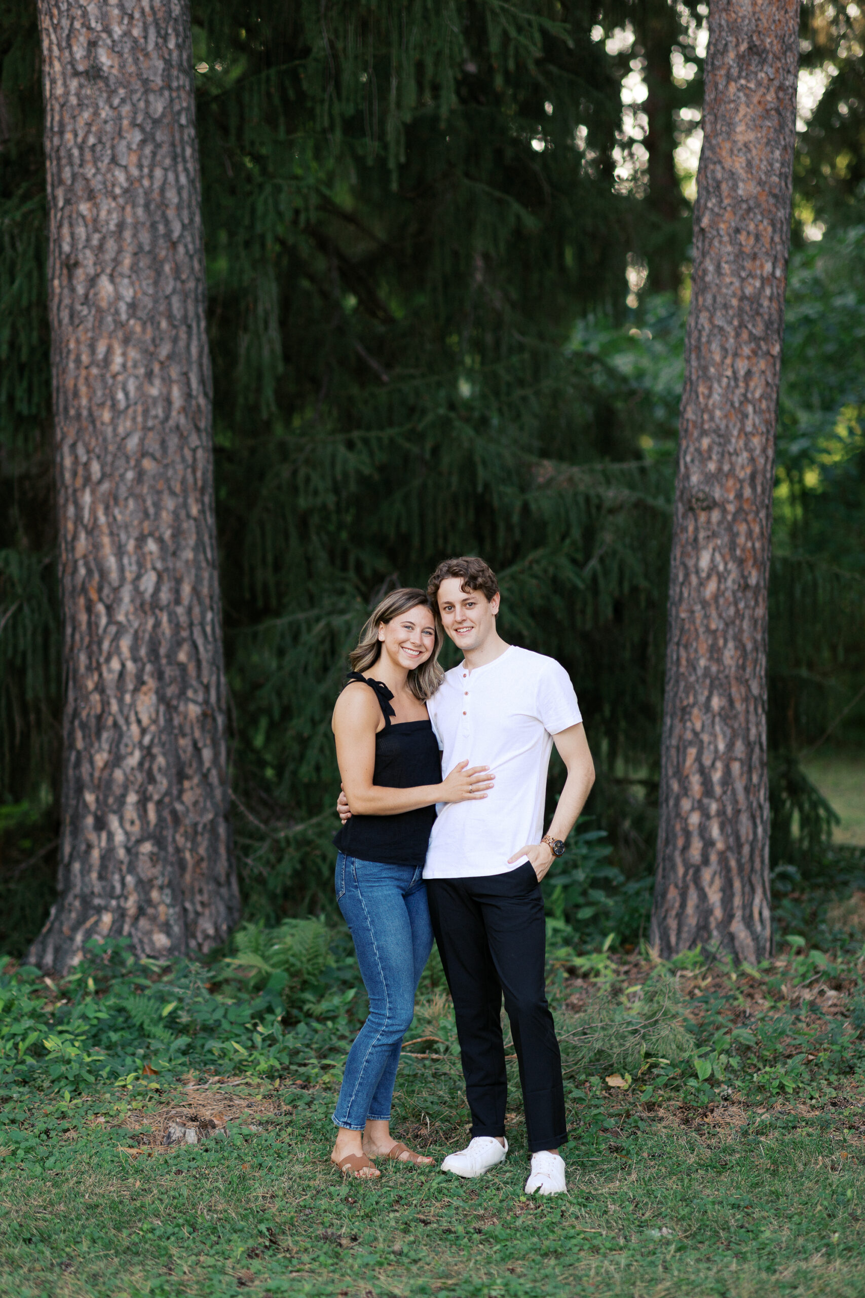 "With his hand in his pocket and her arms wrapped around him, they look into the camera under the tall tree at Noerenberg Gardens. Captured by Toly Dzyuba Photography, your trusted Minnesota wedding photographer.