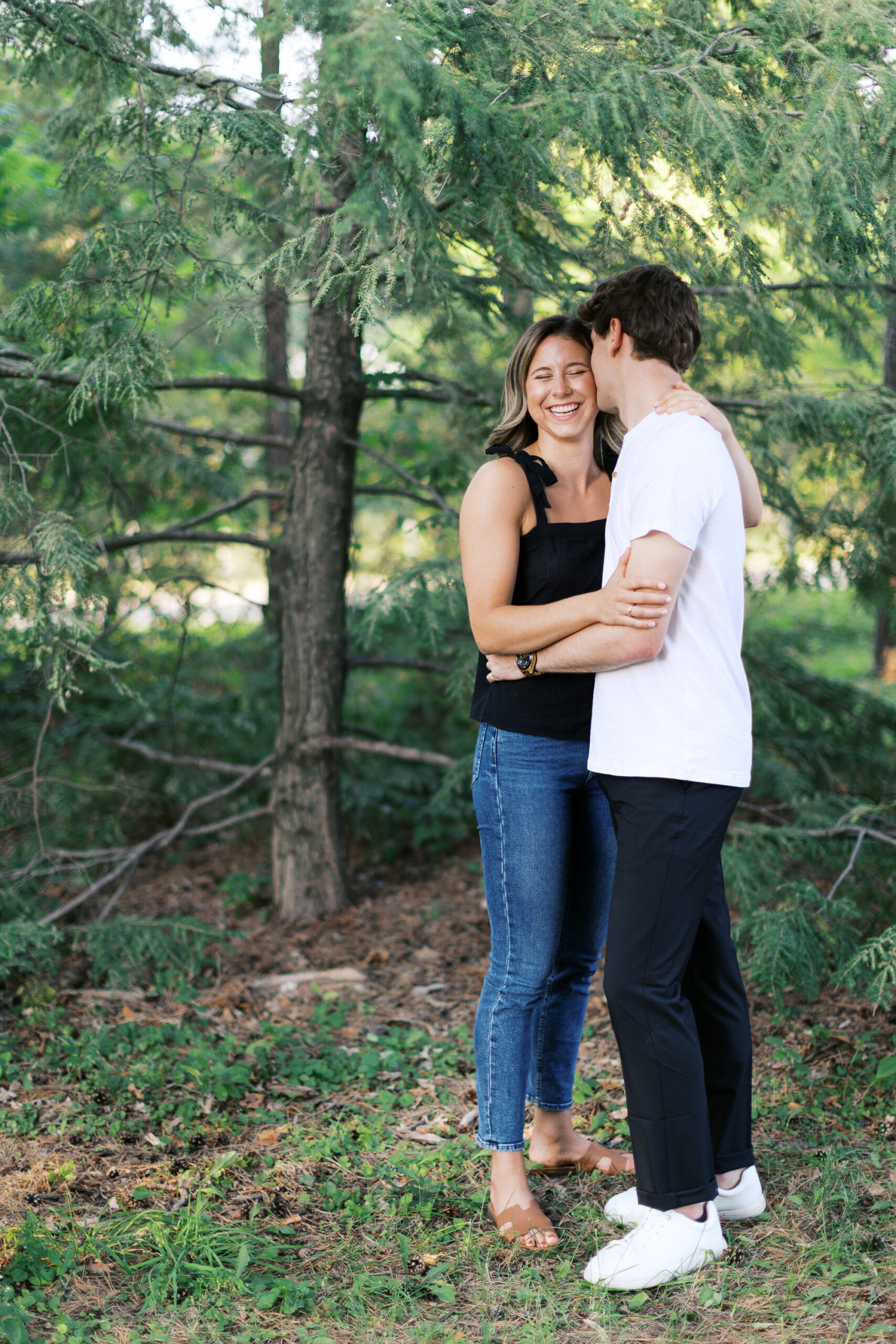 Under the tree, he gently kisses her on the cheek, and they smile in this tender moment. Captured by Toly Dzyuba Photography, your trusted Minnesota wedding photographer.