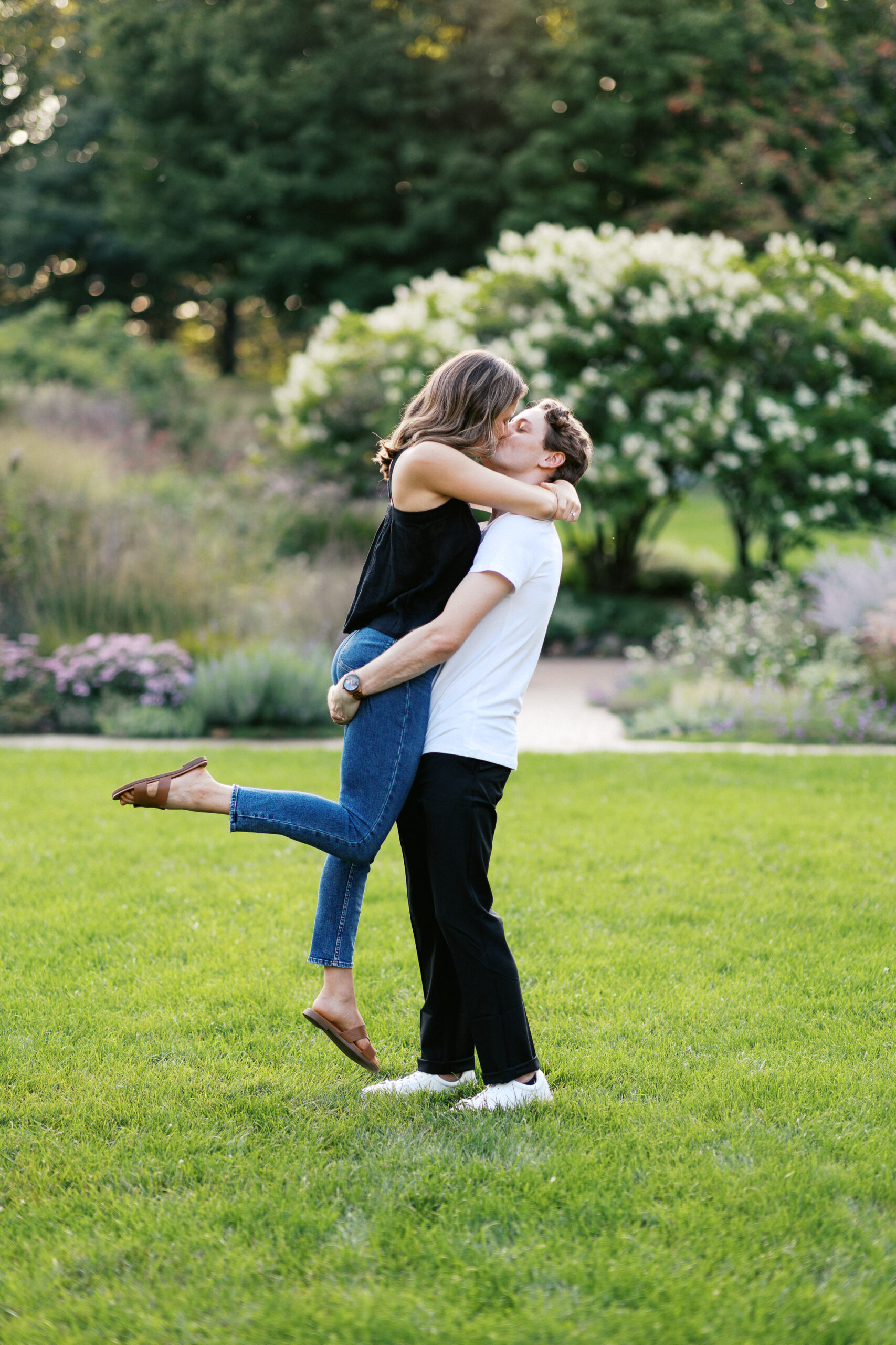 He picks her up and kisses her in the gardens, with the sunset casting a golden glow around them. Captured by Toly Dzyuba Photography.