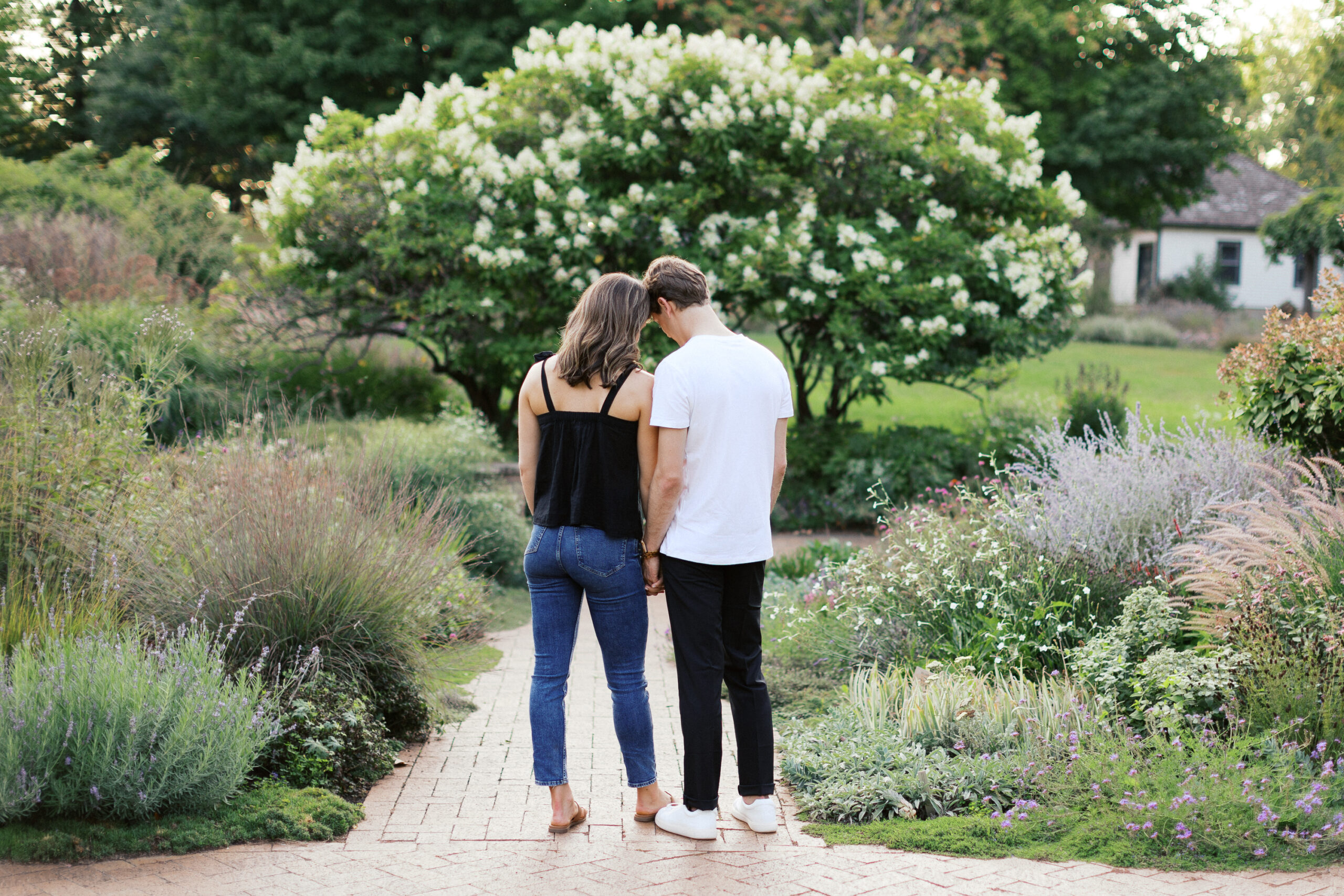 The couple stands in the garden, their heads gently touching as they face away, sharing a quiet, intimate moment. Captured by Toly Dzyuba Photography.