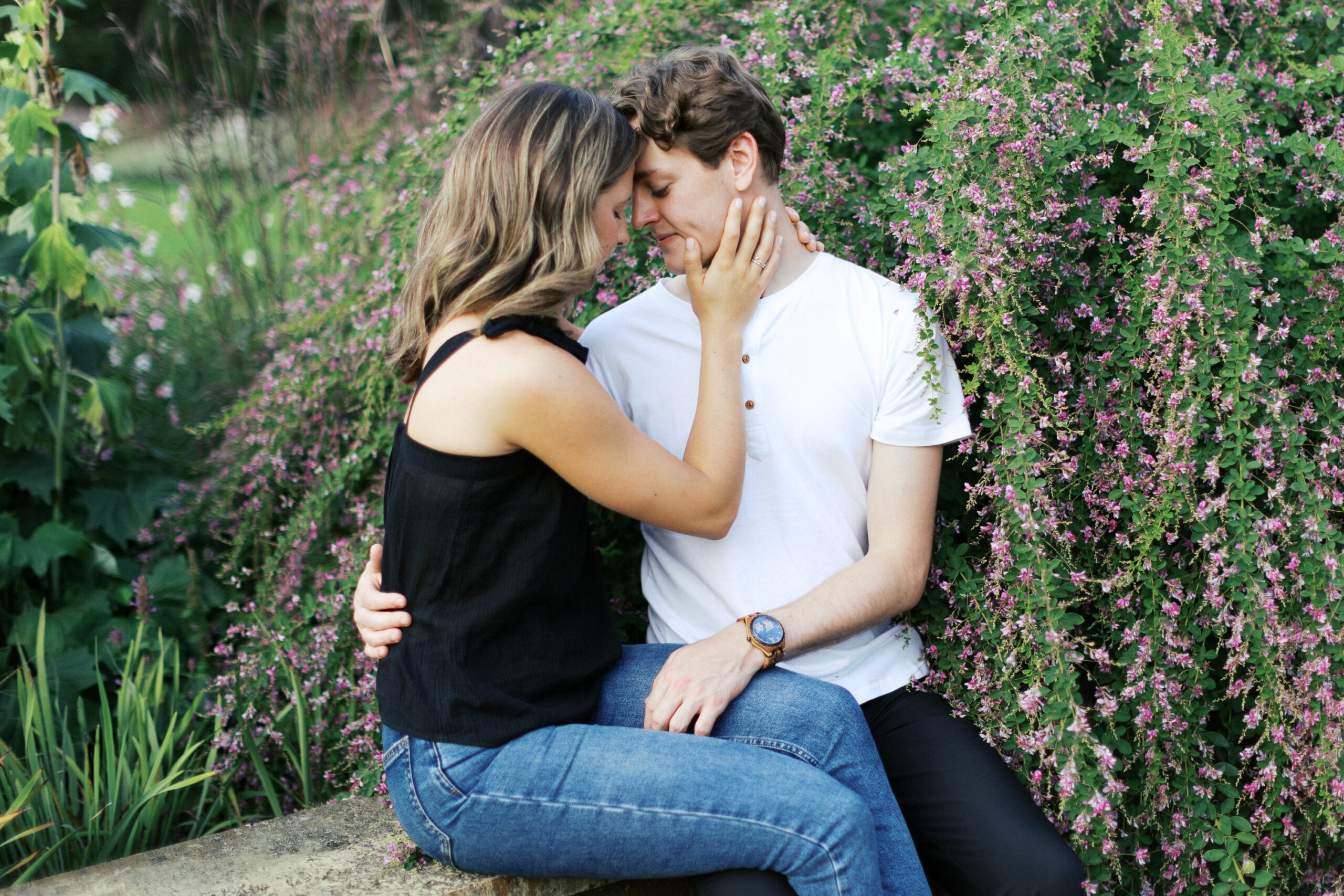 Sitting at Noerenberg Gardens on the edge of a garden wall, the couple gently touches heads, sharing a quiet, intimate moment. Captured by Toly Dzyuba Photography, your trusted Minnesota wedding photographer.