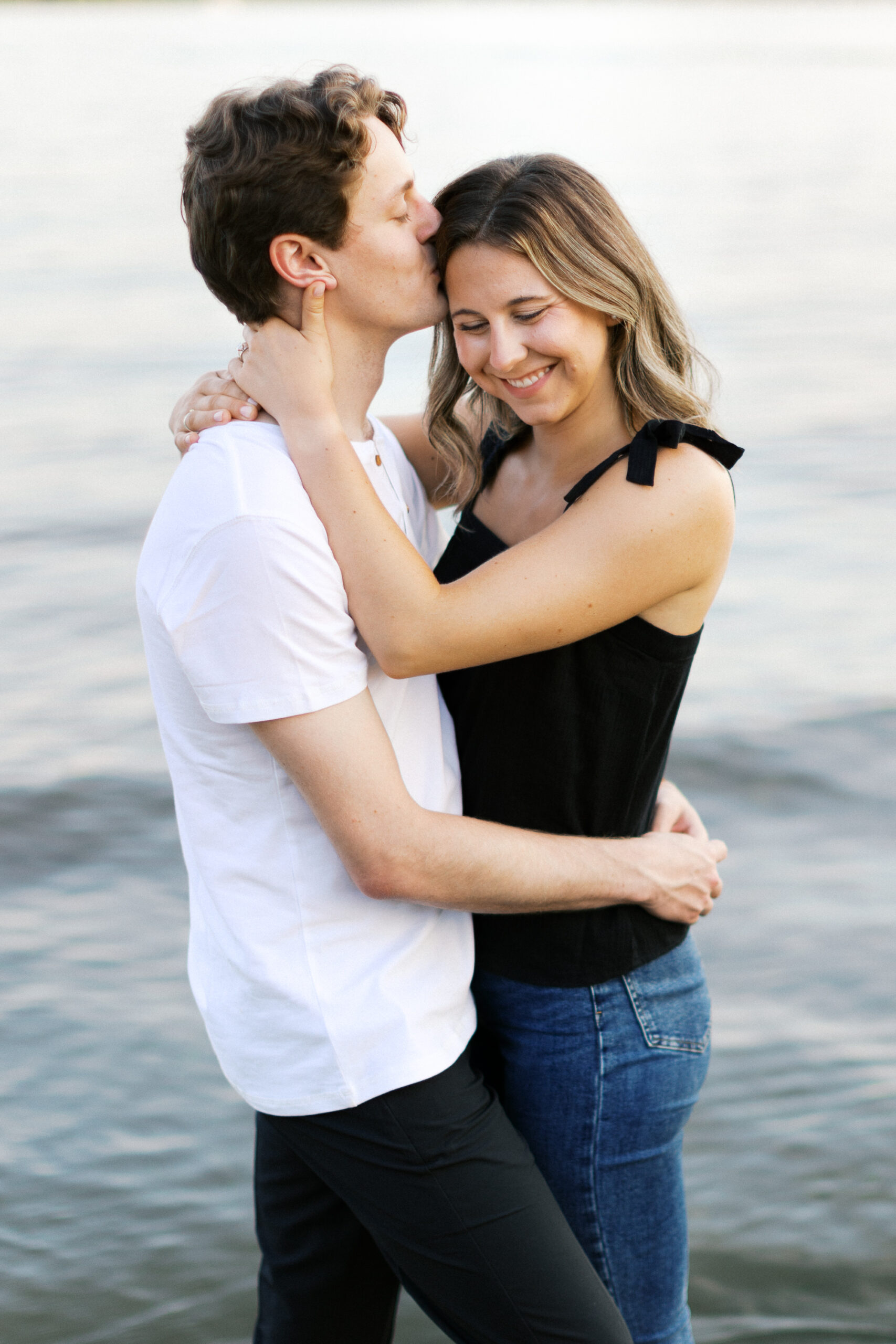 A tender moment in the lake as he gently kisses her head, and she smiles warmly, surrounded by the serene beauty of the water. Captured by Toly Dzyuba Photography.