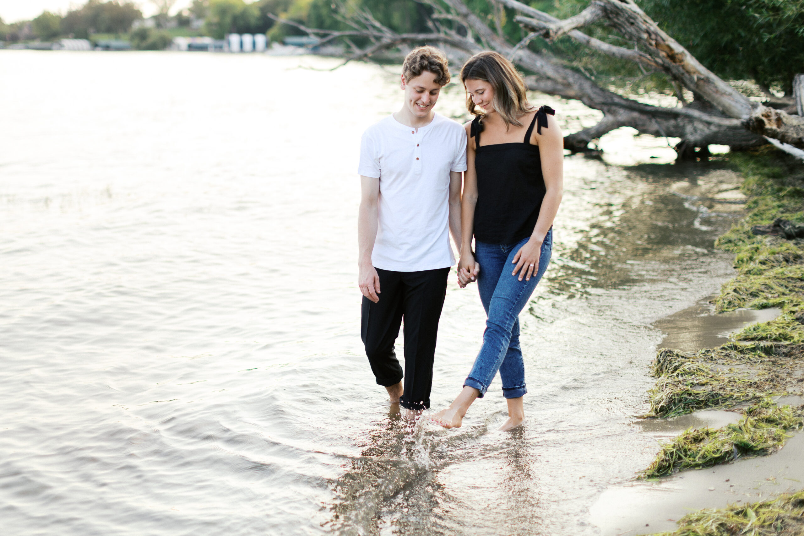 A playful and joyful moment as the couple walks through the lake, she splashes water with her feet while laughing, embracing the fun and romance. Captured by Toly Dzyuba Photography.