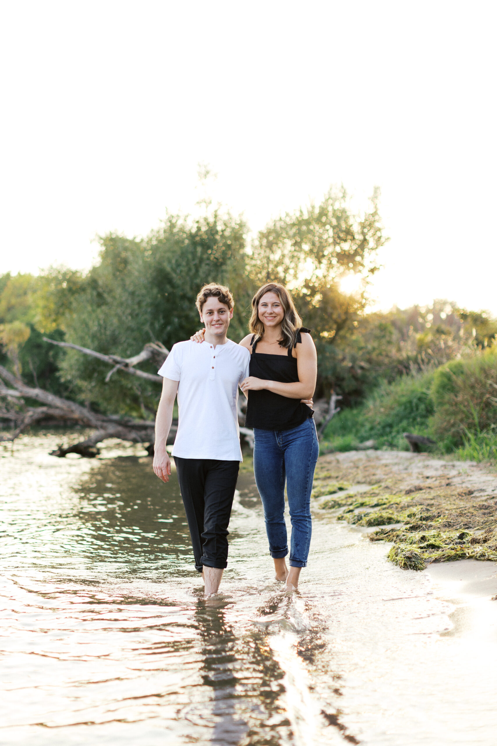 A joyful moment at Noerenberg Gardens as the couple walks through the lake, arms wrapped around each other, smiling at the camera. Captured by Toly Dzyuba Photography.