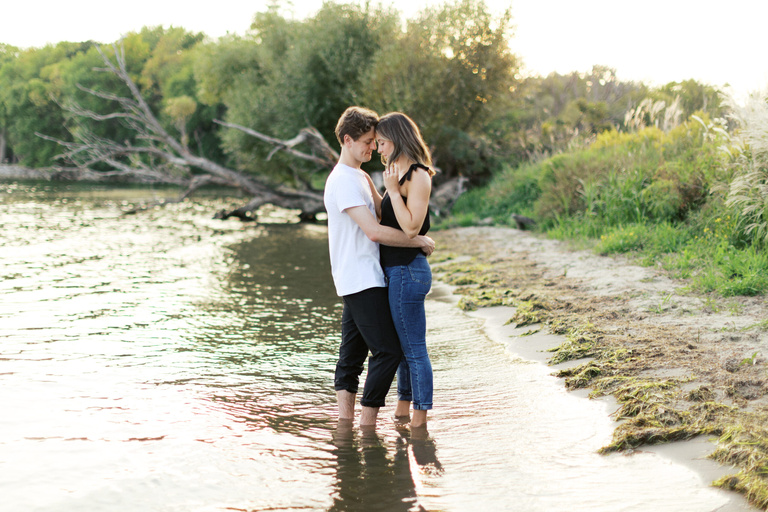 Couple on the beach standing in the Lake Minnetonka embracing in a still moment as sunset showers them both - Engagement session by Lake Minnetonka.