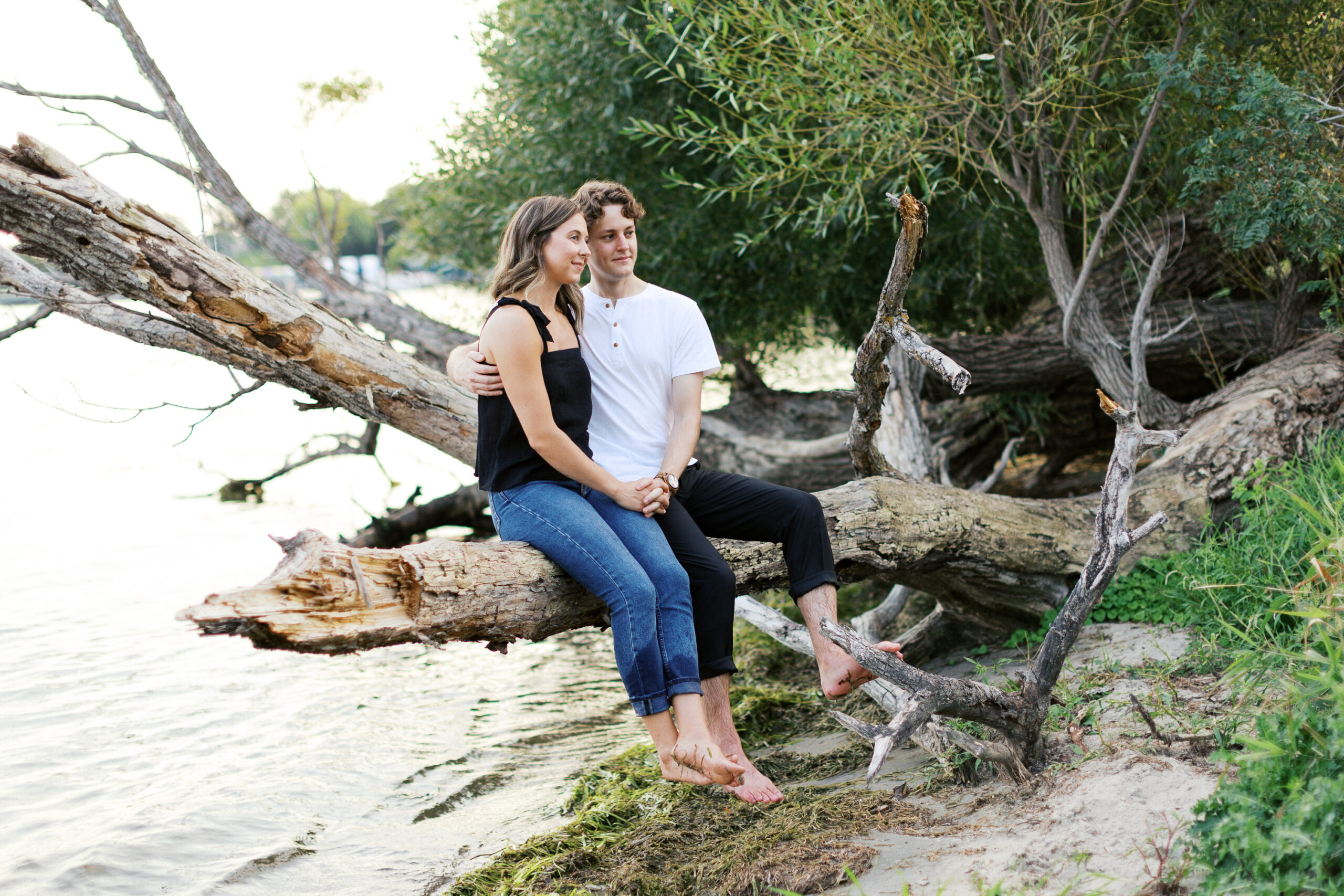 A romantic moment as the couple sits on a broken branch over the lake, embracing each other with warmth and love. Captured by Toly Dzyuba Photography.