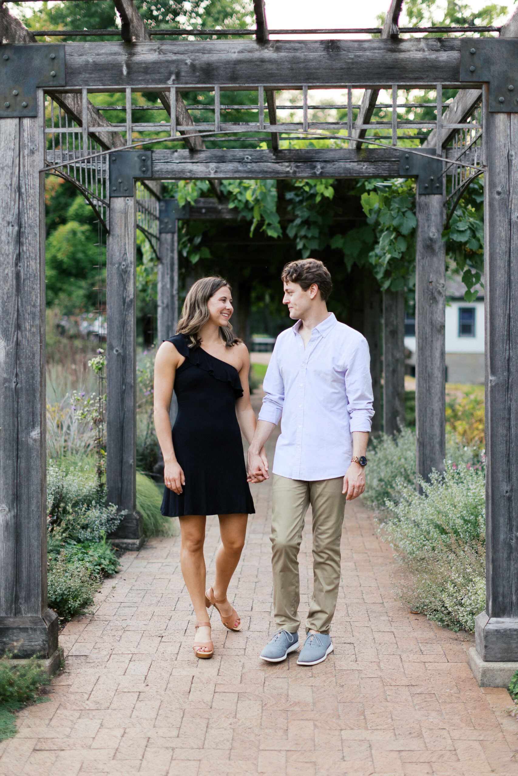 Couple walking and holding hands. Noerenberg Gardens in Orono. Captured by Toly Dzyuba Photography.