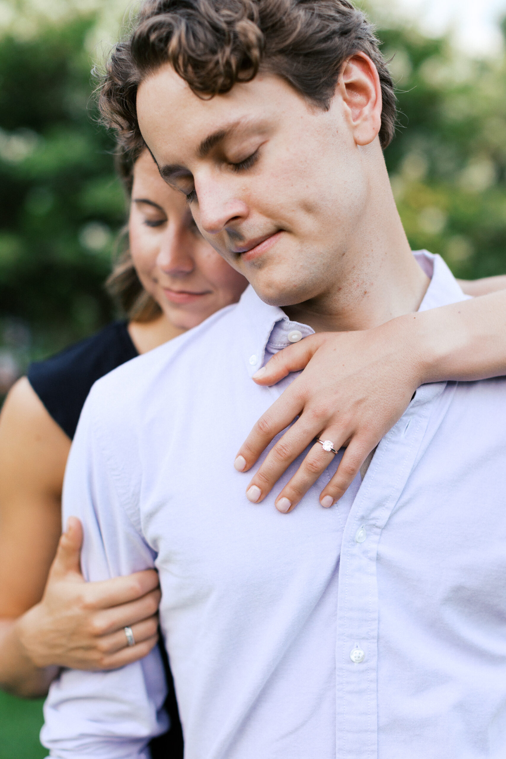 She has her arm over his shoulder with the engagement ring showing. 