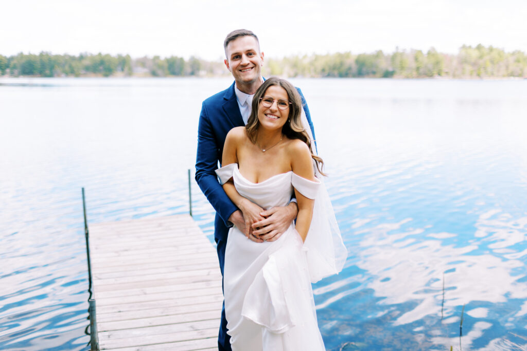 Groom standing on the dock hugging his bride and smiling. Nature Link Resort in Minnesota.