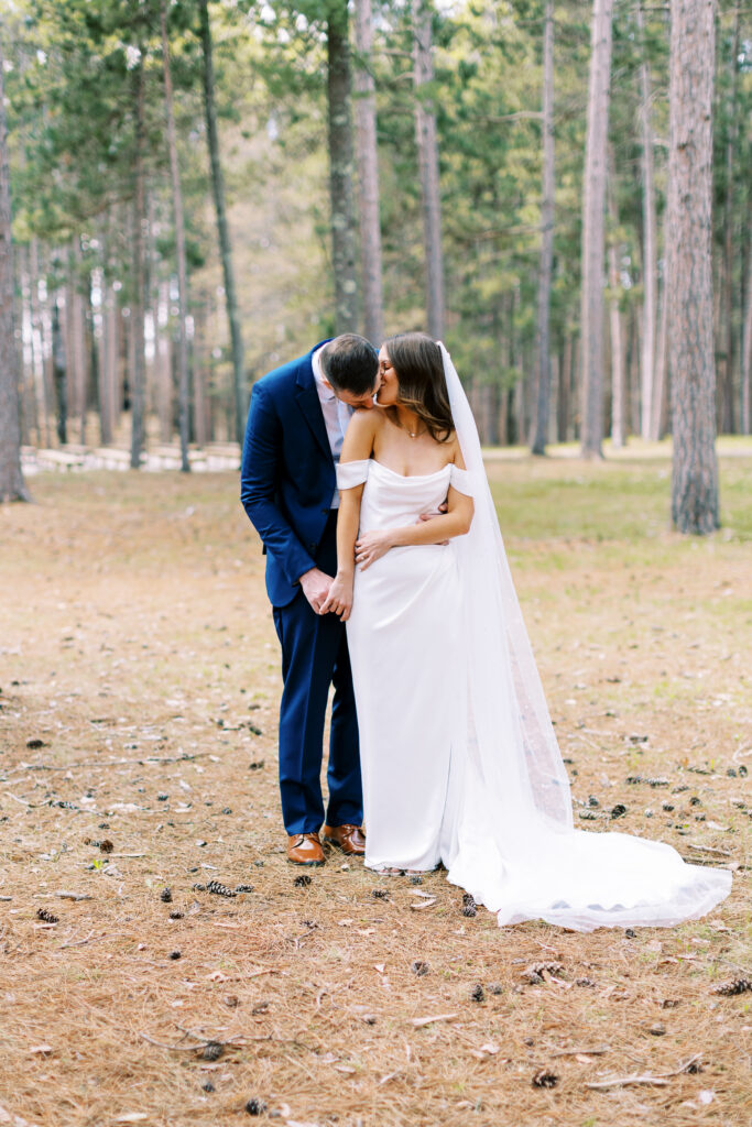 Groom gently kissing her shoulder surrounded by pine trees at catalyst by nature link resort.