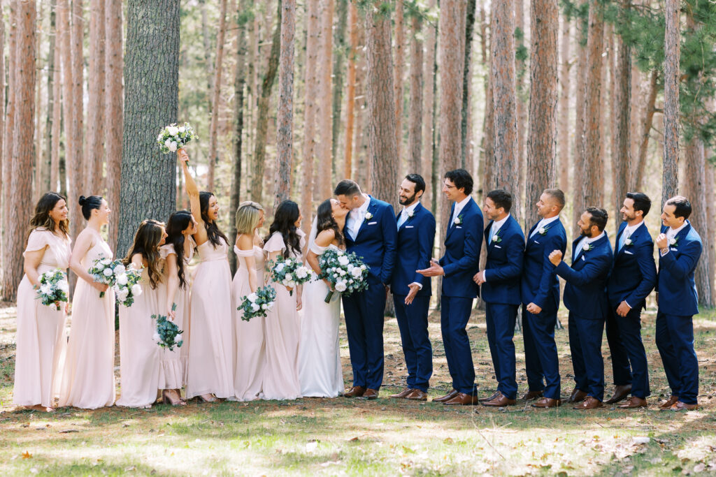 Wedding party watches while the bride and groom kiss and everyone is cheering. Minnesota wedding photographer. 