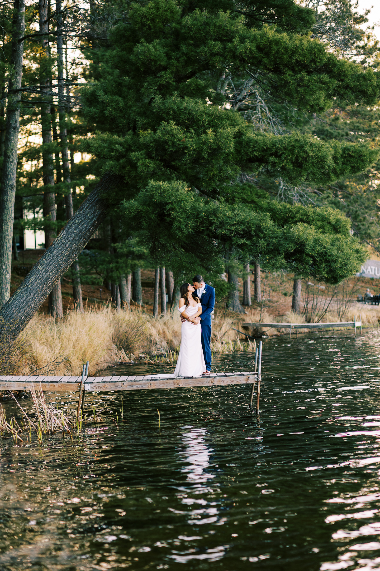 Bride and groom standing on the dock overlooking the beautiful lake at Catalyst at Nature Link. Captured by Minnesota wedding photographer -Toly Dzyuba Photography. Alt text.